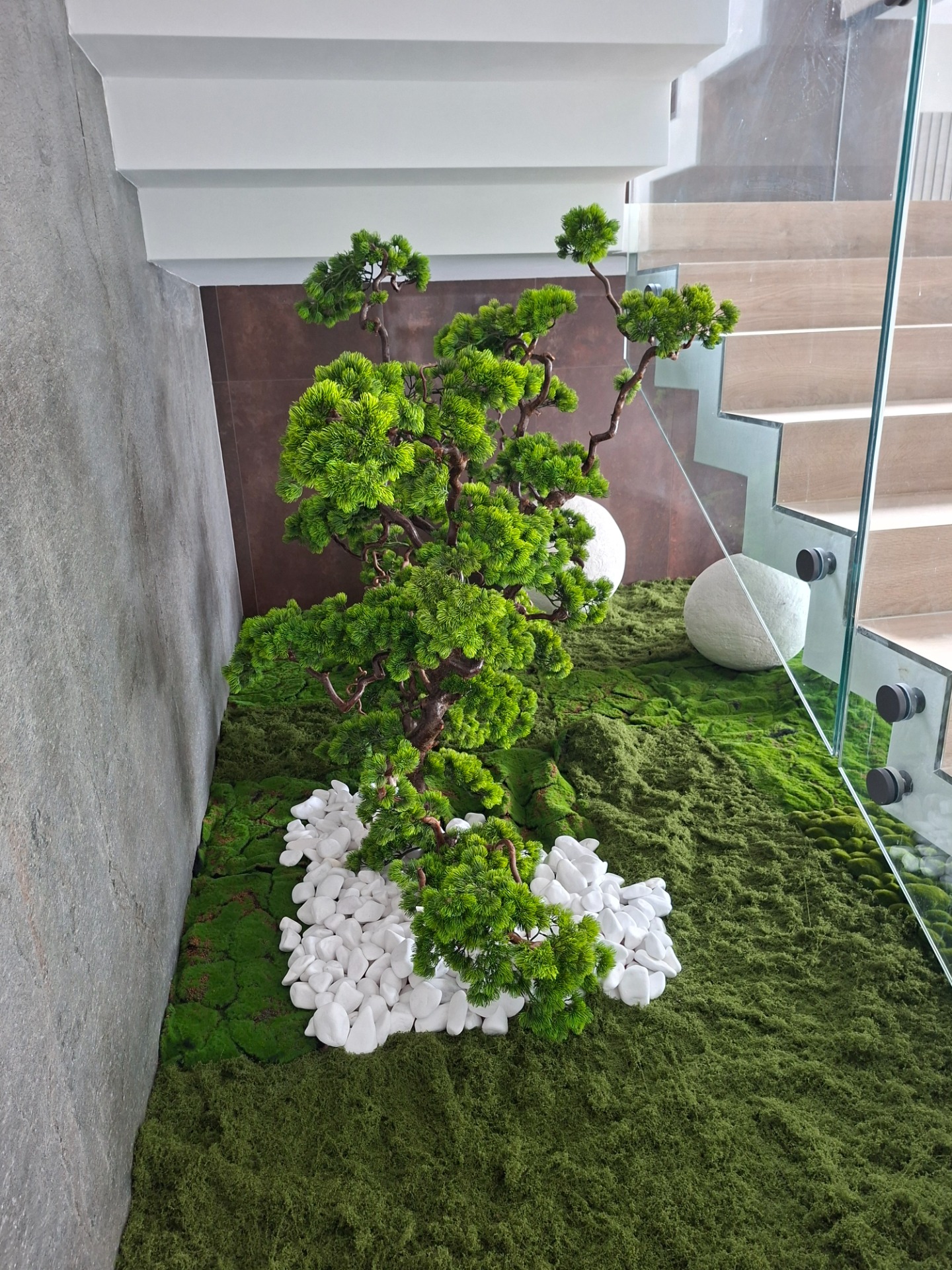 🌿Egyedi, gondozásmentes zöld megoldásokat keres modern enteriőrökbe? 🪾Valódi fa törzsre épülő,  kompozícióim  tökéletes választást jelentenek a nehezen benapozott vagy karbantartást nem igénylő terekbe .  A stabilizált mohaágyás és a prémium műfenyő kombinációja  exkluzív, japán ihletésű hangulatot teremt a legigényesebb projektekben is .   🪾Valódi fatörzs: A törzs rusztikus, természetes megjelenés , egy valódi, újrahasznosított fatörzs , ami prémium és élethű hatást kölcsönöz a műbonsainak.  👌Gondozásmentes: Az ilyen típusú műnövények legnagyobb előnye, hogy nem igényelnek öntözést, fényt vagy bármilyen karbantartást, mégis megőrzik friss megjelenésüket.  ✨️Modern dizájn: A minimalista belsőépítészettel, a szürke falakkal, a fa lépcsőkkel és az üveg korláttal együtt egy nagyon letisztult, japán ihletésű, modern enteriőr.  A fehér kavicsok kontrasztot adnak a zöld mohaágyással.   Válasszon egyedi tervezésű, kézzel készített dekorációt, amely  megőrzi frissességét. Gondozásmentesen 