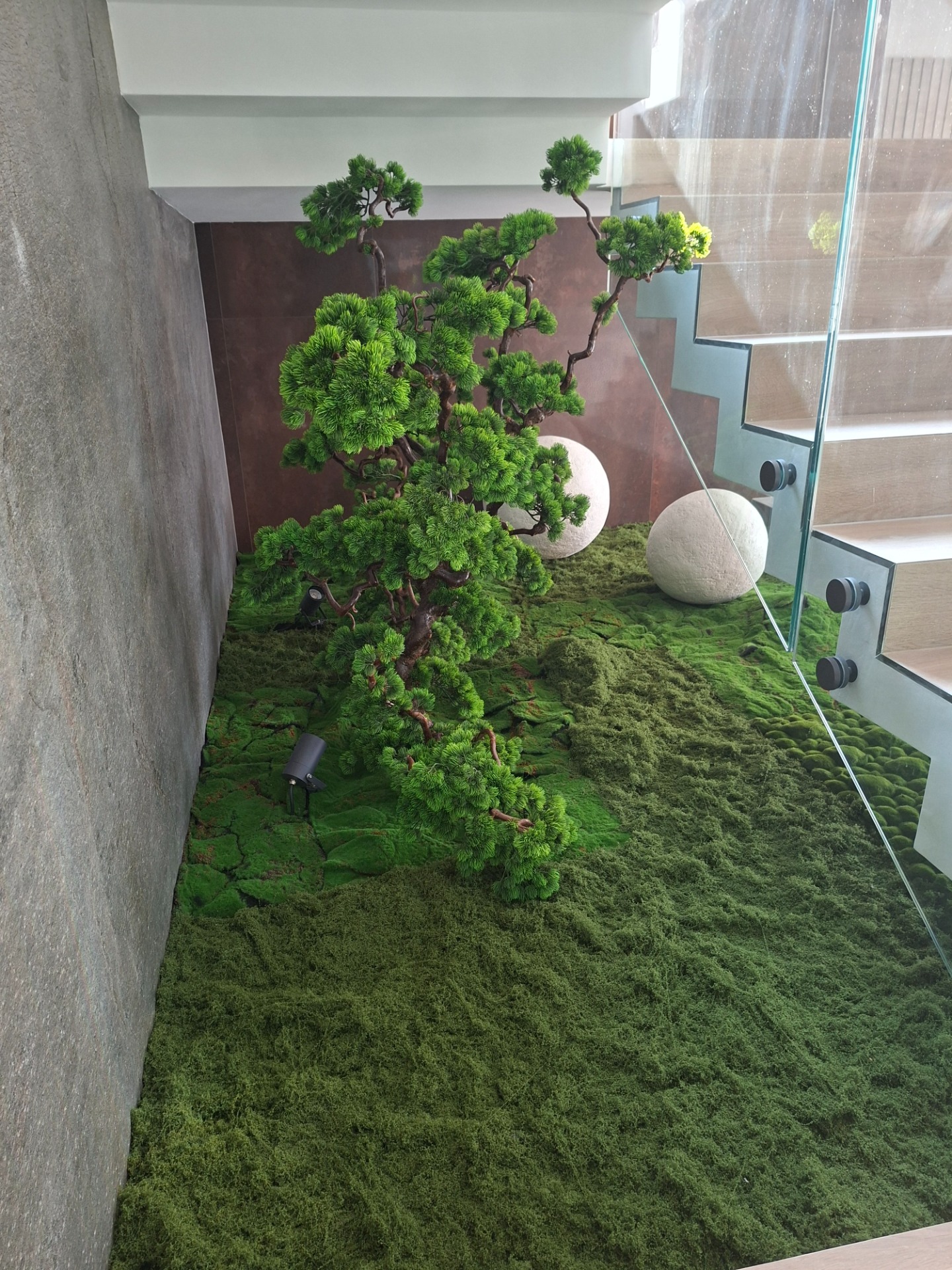 Egyedi, gondozásmentes zöld megoldásokat keres modern enteriőrökbe? Valódi fa törzsre épülő, kompozícióim tökéletes választást jelentenek a nehezen benapozott vagy karbantartást nem igénylő terekbe . A stabilizált mohaágyás és a prémium műfenyő kombinációja exkluzív, japán ihletésű hangulatot teremt a legigényesebb projektekben is . Valódi fatörzs: A törzs rusztikus, természetes megjelenés , egy valódi, újrahasznosított fatörzs , ami prémium és élethű hatást kölcsönöz a műbonsainak. 👌Gondozásmentes: Az ilyen típusú műnövények legnagyobb előnye, hogy nem igényelnek öntözést, fényt vagy bármilyen karbantartást, mégis megőrzik friss megjelenésüket. ✨️Modern dizájn: A minimalista belsőépítészettel, a szürke falakkal, a fa lépcsőkkel és az üveg korláttal együtt egy nagyon letisztult, japán ihletésű, modern enteriőr.